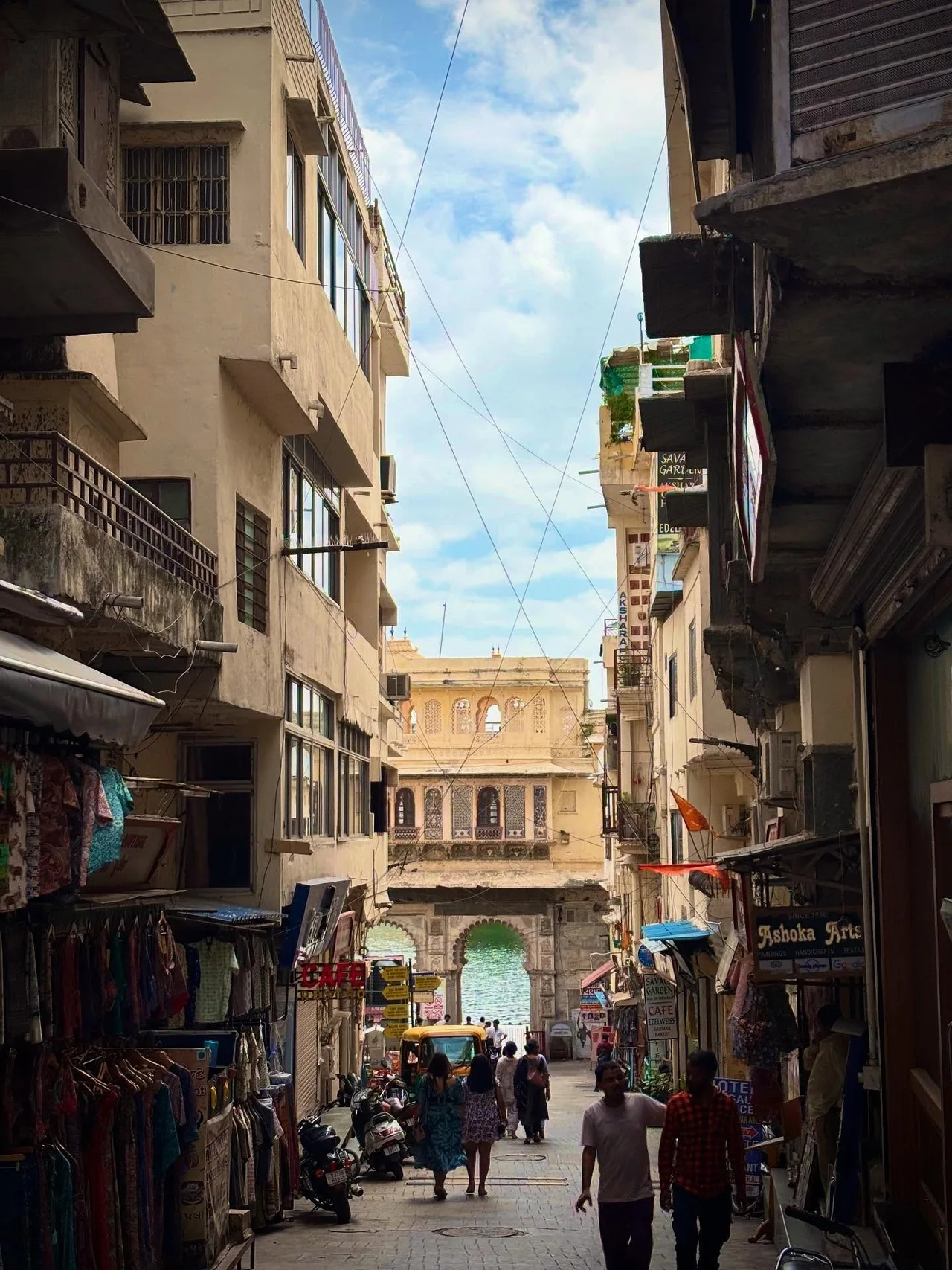 A narrow shopping street leading down to a gateway and lake in Udaipur.